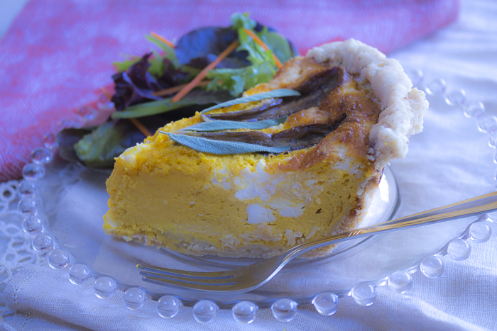 A wedge of quiche with chunks of goat cheese inside a velvety squash custard - eggplant is baked on top