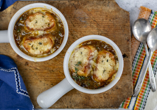 Classic french Onion Soup in white modern crocks on a wooden board with vintage linens