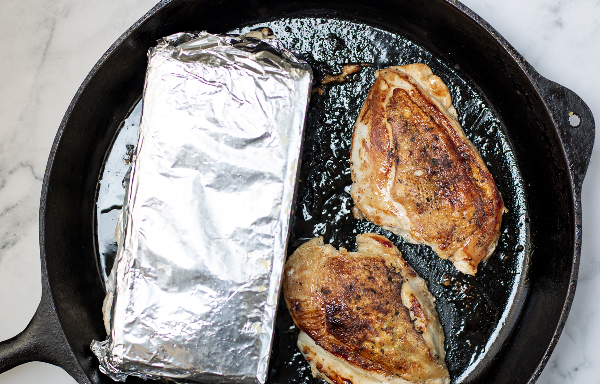  chicken breasts in a cast iron skillet with skin side down using two bricks a weights 