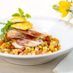 Sliced brick chicken breast on a Summer vegetable ragout in white bowl