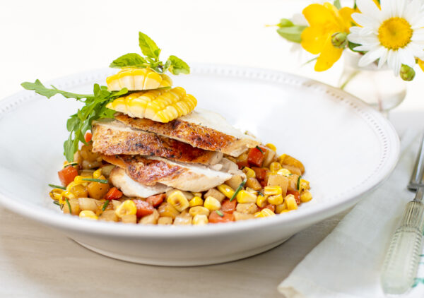 Sliced brick chicken breast on a Summer vegetable ragout in white bowl