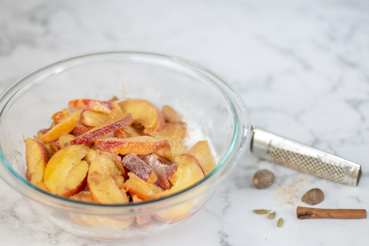 Sliced peaches in a bowl for pie with nutmeg, cinnamon and cardamom