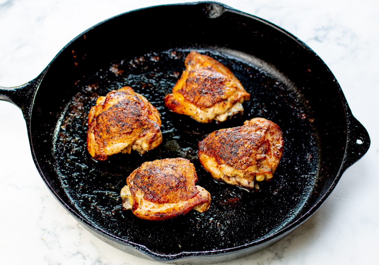 Searing the seasoned chicken thighs in a cast iron skillet