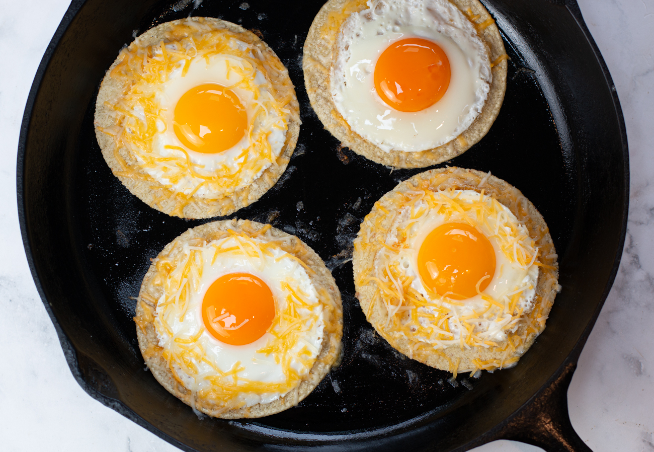 Adding fried eggs to tortilla with Mexican cheeses